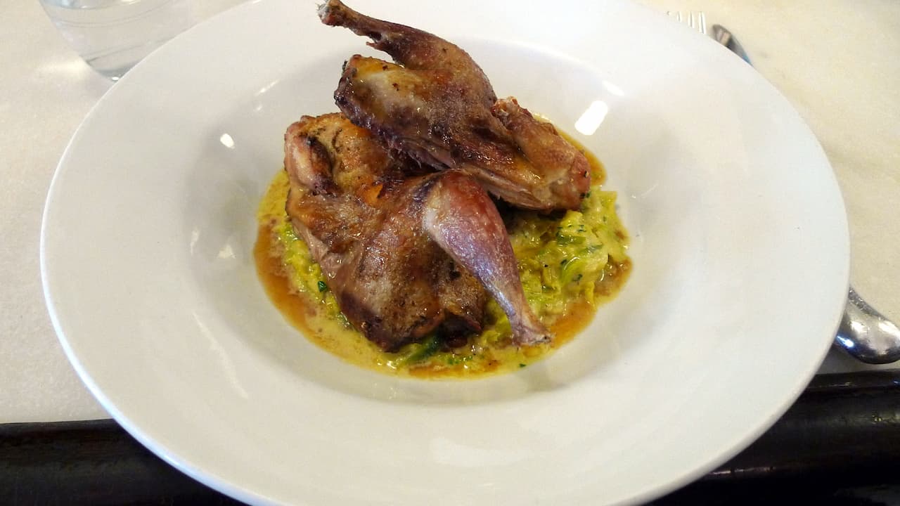 Roasted game bird served on a bed of creamy vegetable mash in a white bowl