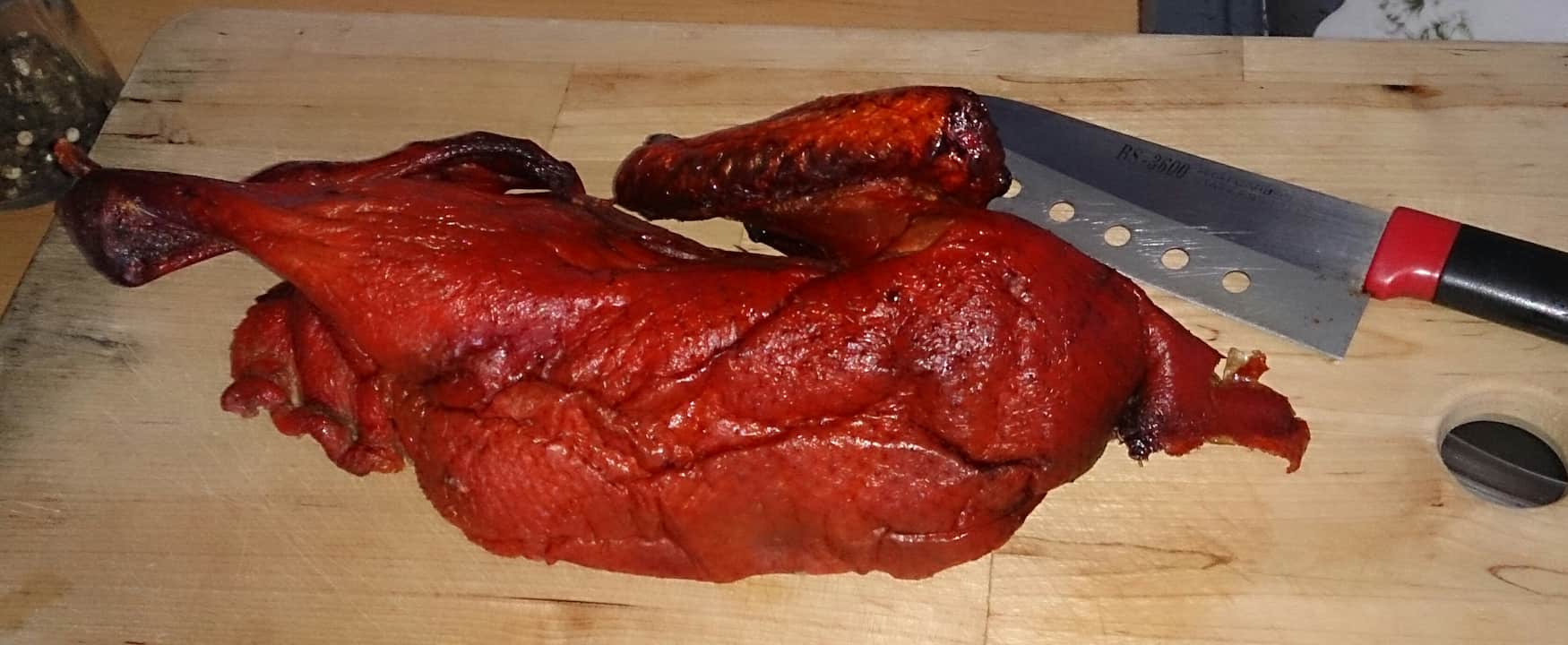 Whole roasted duck with crispy red-brown skin on a wooden cutting board next to a knife