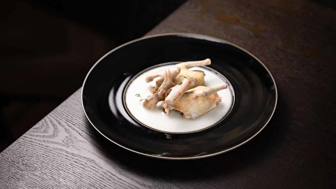 Gourmet presentation of two poached quail served on a black-rimmed white plate