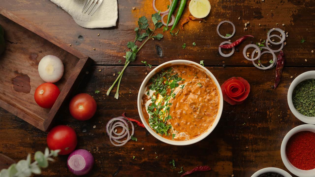 Masaman curry in a bowl garnished with cilantro, surrounded by raw ingredients and spices on a rustic table