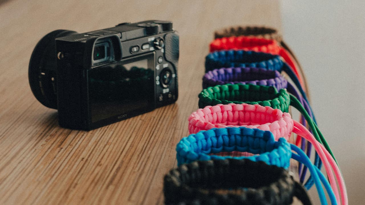 A digital camera on a wooden surface beside colorful paracord bracelets