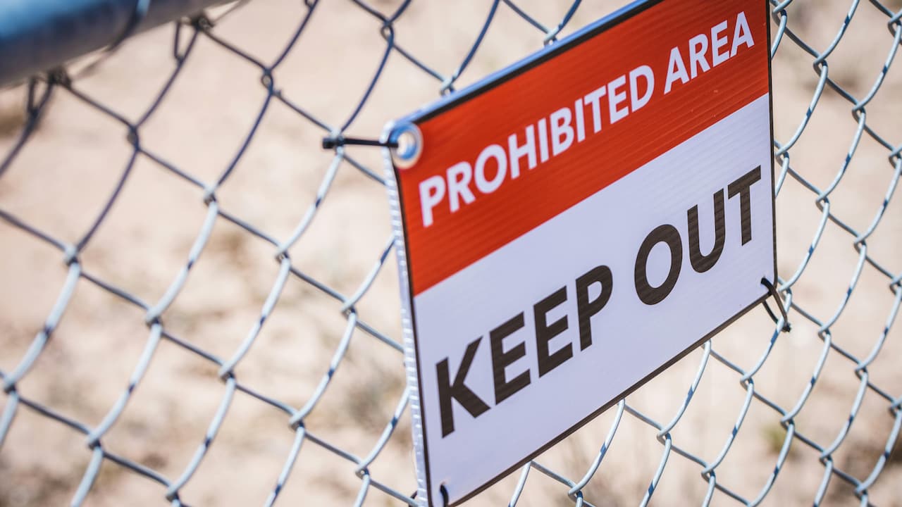 "PROHIBITED AREA KEEP OUT" sign attached to a chain-link fence