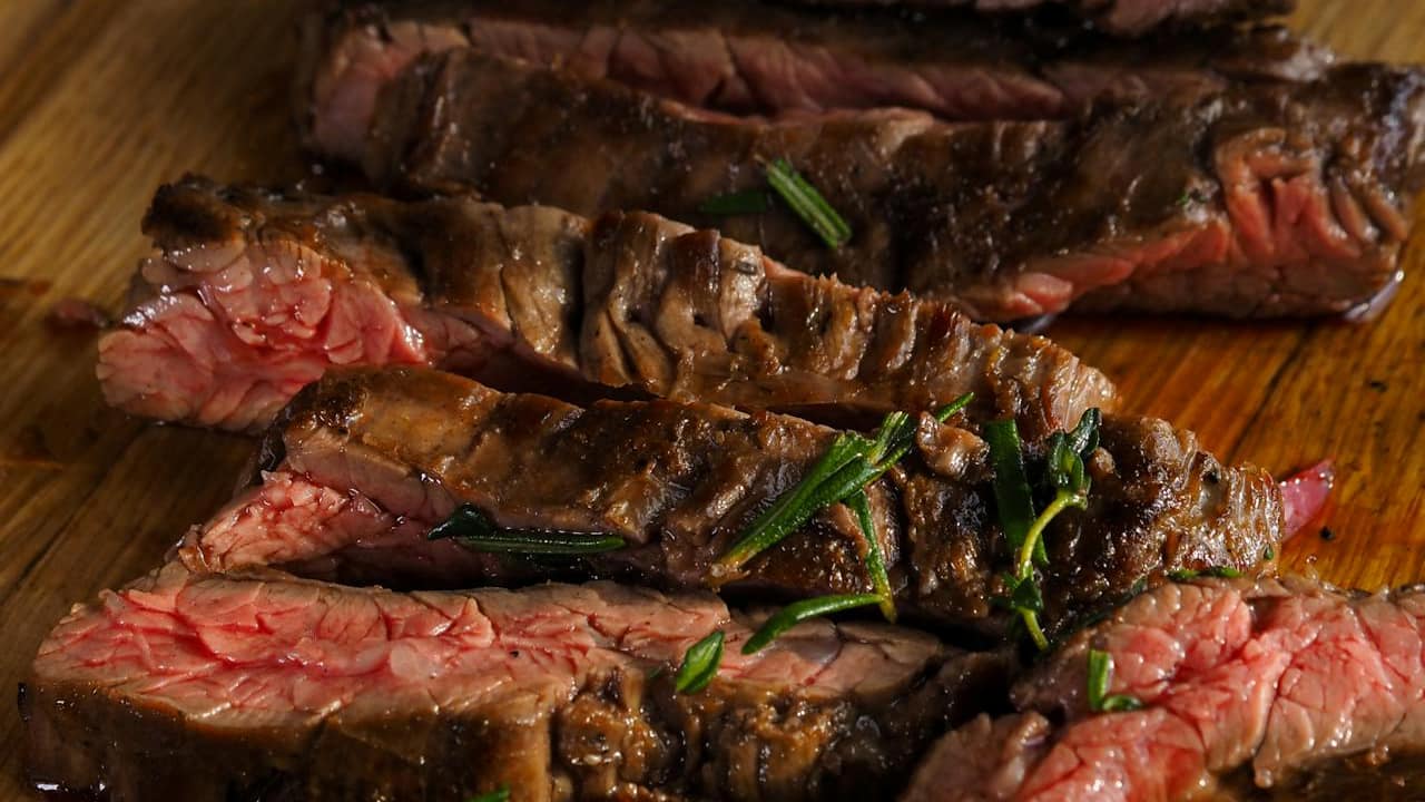 Medium-rare grilled steak slices garnished with herbs on a wooden cutting board