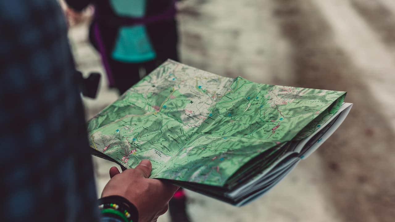 Person holding a topographic map outdoors with trails and terrain visible