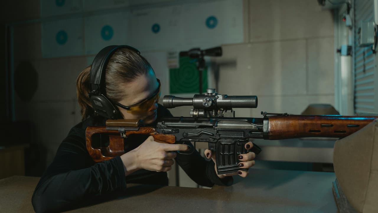 Woman aiming a scoped rifle at an indoor shooting range