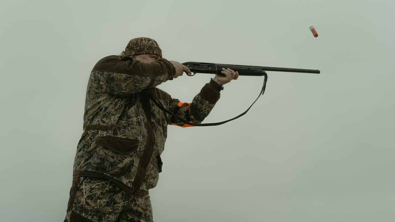 Hunter firing shotgun with shell mid-air