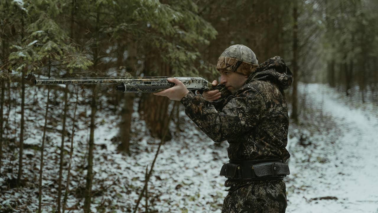 Hunter in camouflage aiming a shotgun in a snowy forest
