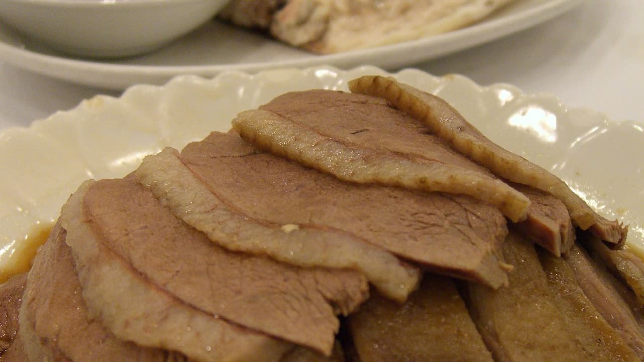 Thinly sliced braised goose breast arranged in overlapping layers on a white ceramic plate