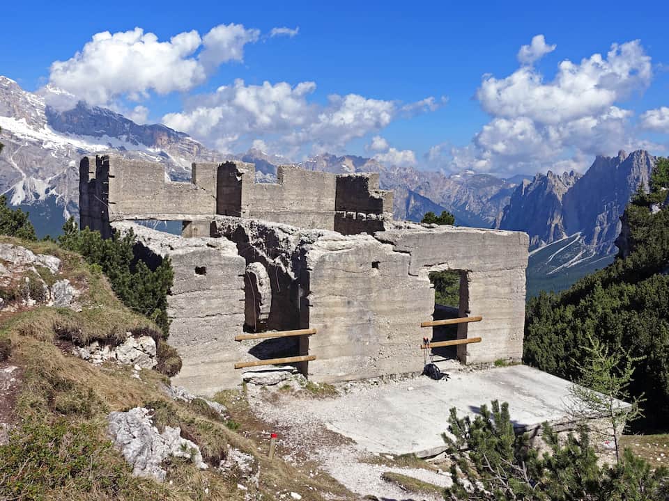 Crumbling concrete building ruin on a mountain ledge along Cliffhanger Trail with jagged alpine peaks in the background