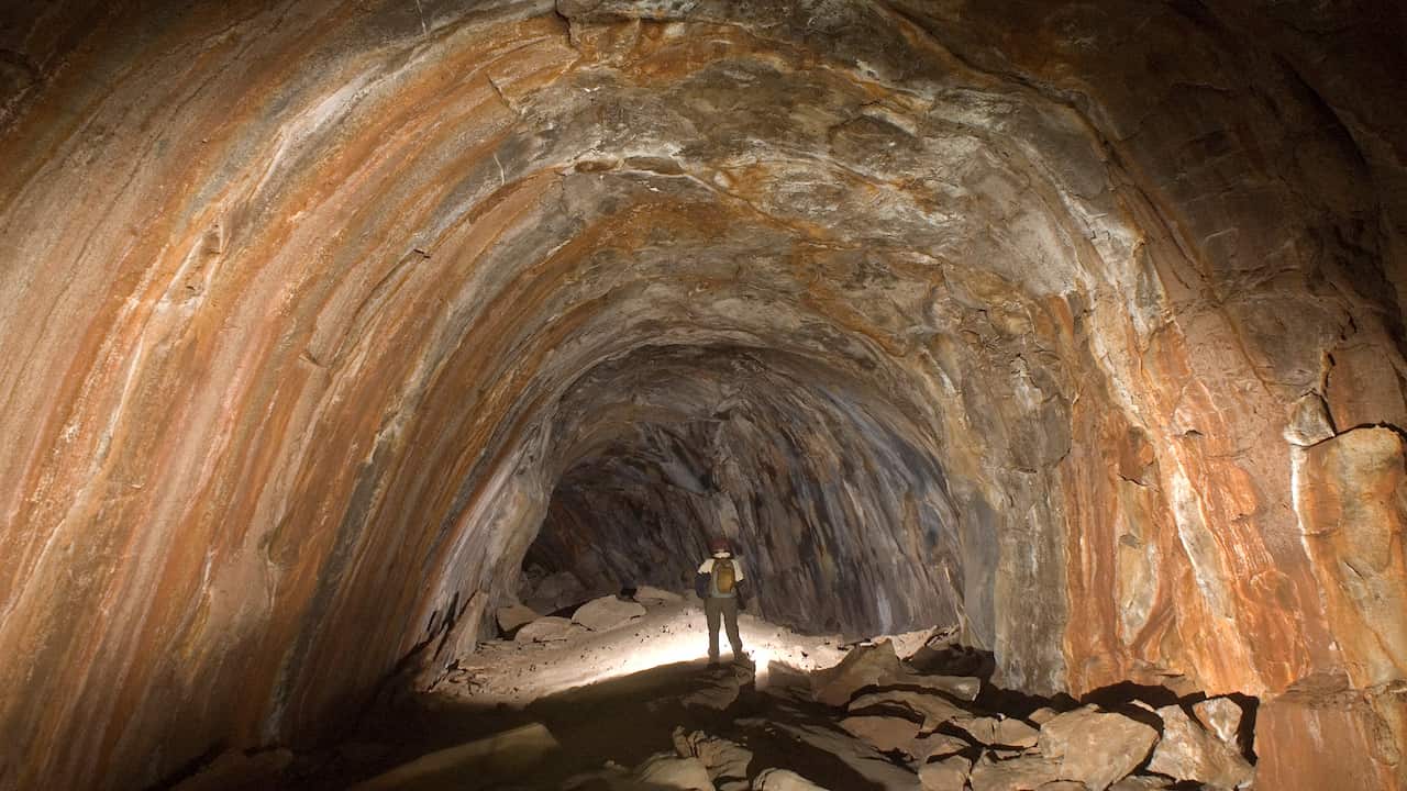 Hiker exploring a dimly lit tunnel with layered volcanic rock walls in Hidden Cave System Trails, Arizona