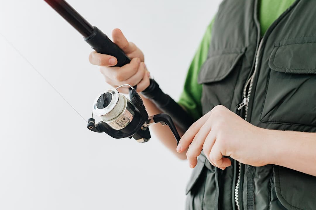 Person in a green vest holding and adjusting a fishing rod and reel