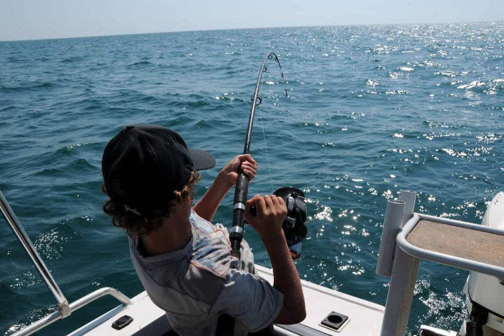 Person on a boat holding a fishing rod, reeling in a catch over open water