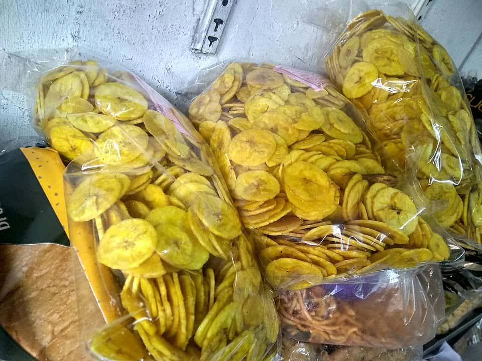Several clear plastic bags filled with crispy yellow banana chips stacked upright on a shelf