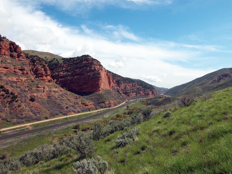 Scenic view of Echo Canyon Trail with red rock cliffs and green hills under a blue sky