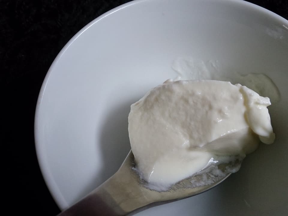 Spoonful of thick, creamy Greek yogurt held over a white bowl