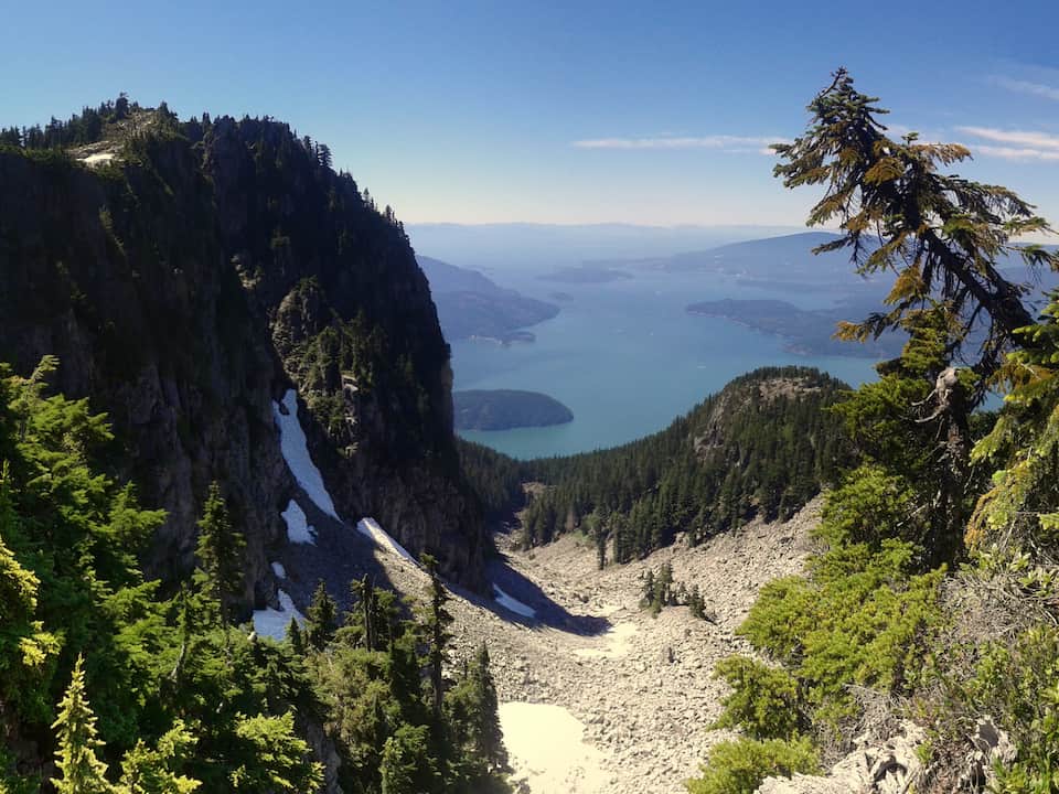 Mountain pass with snow patches overlooking Howe Sound and forested islands under a clear sky