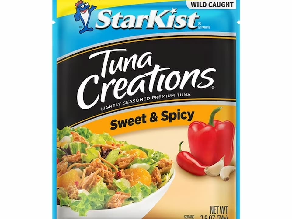 StarKist Tuna Creations Sweet & Spicy pouch, featuring an image of a tuna salad with lettuce and mandarin slices, alongside red bell pepper and garlic cloves, labeled “Lightly Seasoned Premium Tuna” and “Wild Caught”