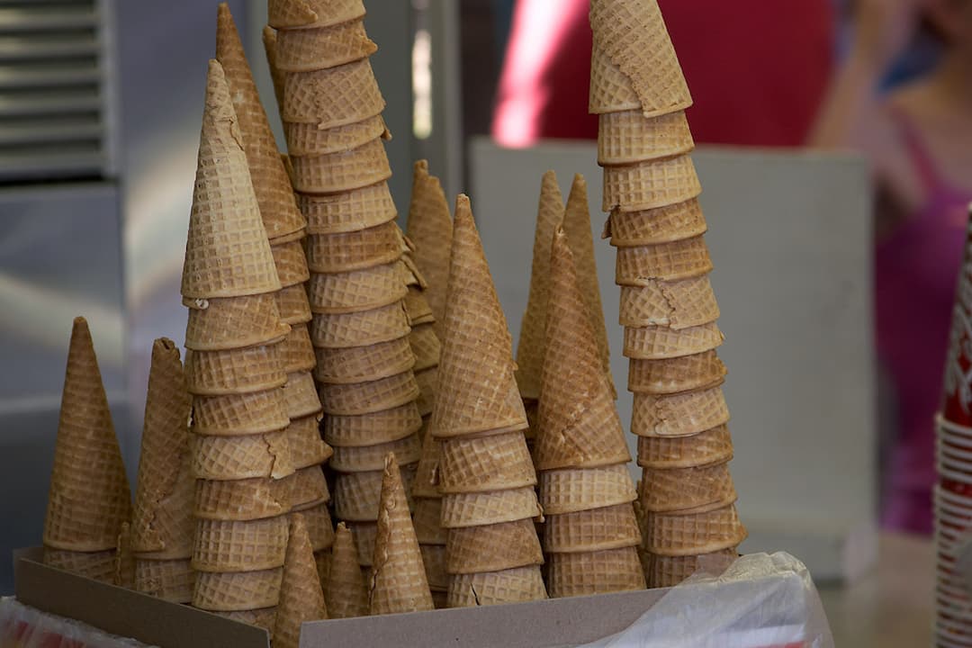 Stacks of waffle-textured sugar cones arranged upright in a cardboard tray at an ice cream stand