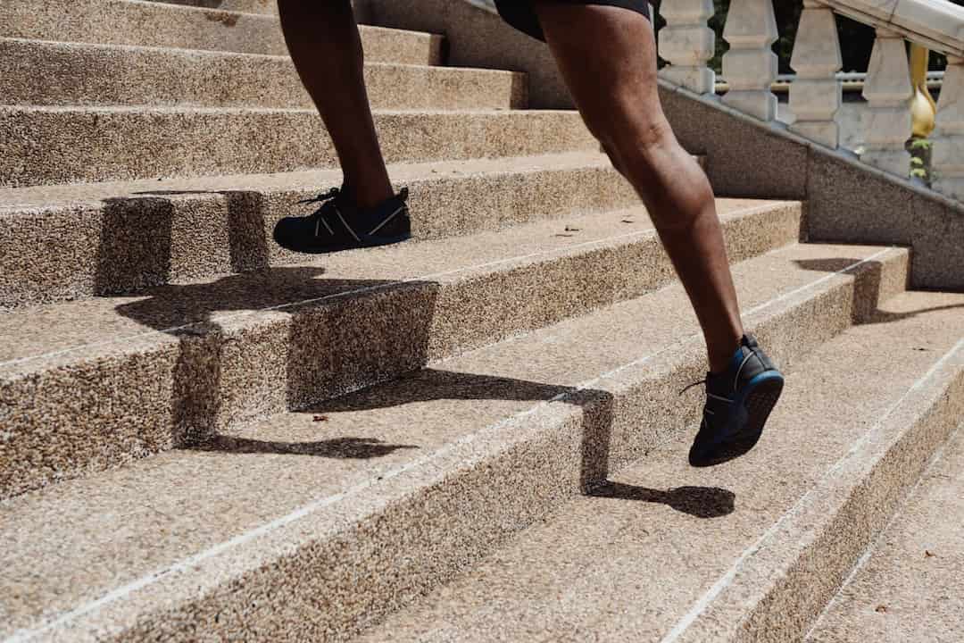 Person running up outdoor stone steps, wearing black athletic shoes and shorts, with shadow cast on the stairs