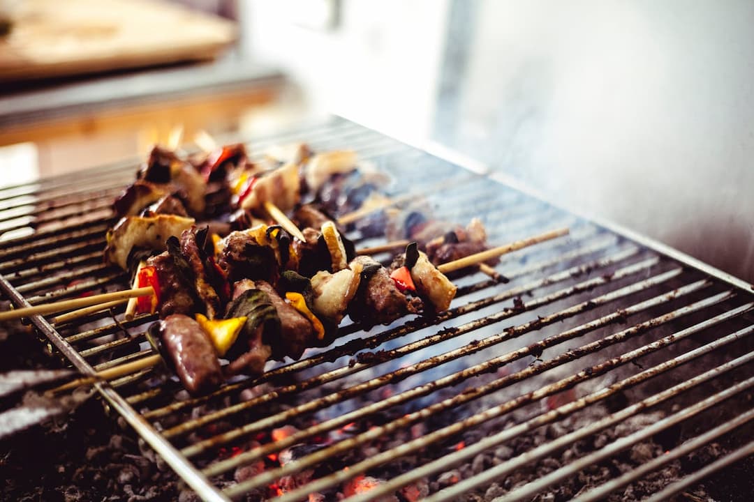 Skewers of grilled meat and vegetables cooking over a hot charcoal barbecue grill, with visible smoke and glowing embers