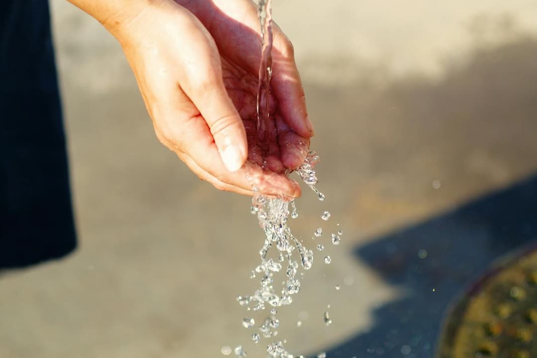 Close-up of hands cupped together, catching flowing water from a faucet or stream, droplets splashing mid-air, sunlight casting gentle highlights on skin and water