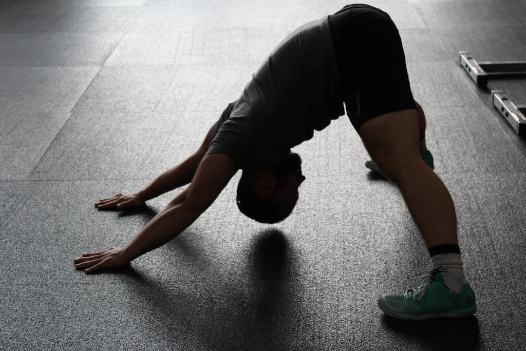 Man in athletic wear performing a downward dog stretch on a gym floor, with arms and legs extended and hips raised