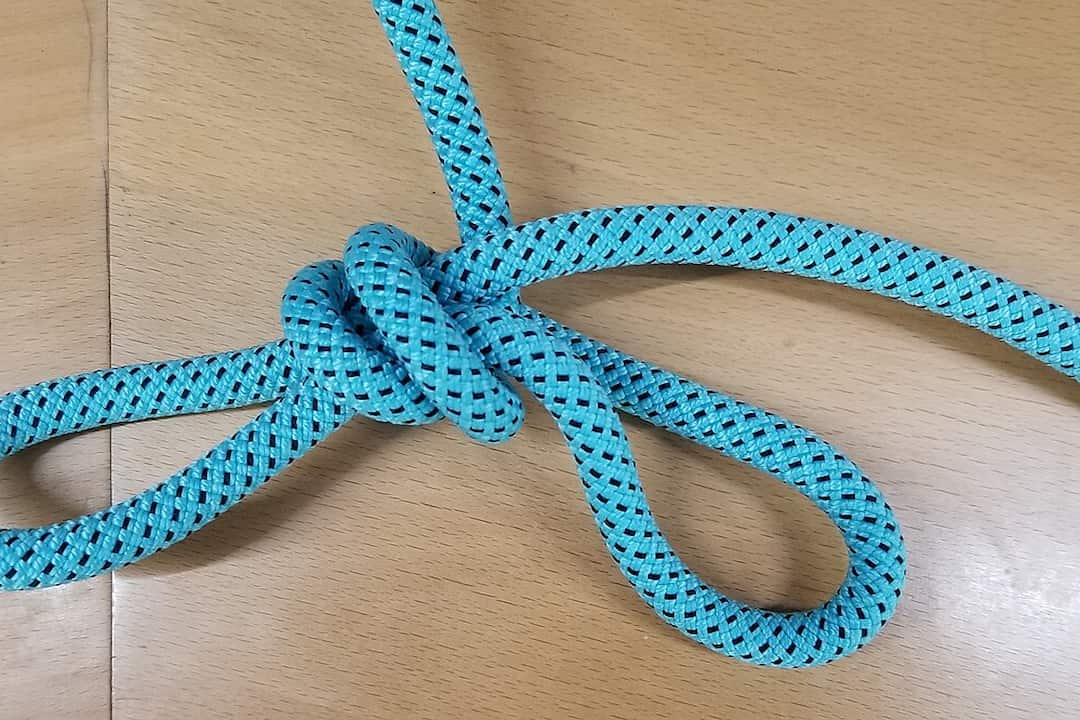 Blue rope tied in a trucker’s hitch knot on a wooden surface, forming two loops and a central tensioning knot