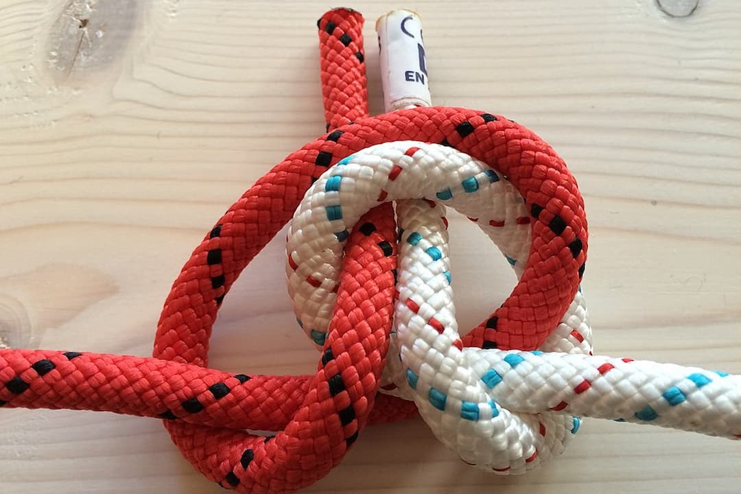 Red and white ropes tied together using an alpine butterfly bend knot on a light wooden surface