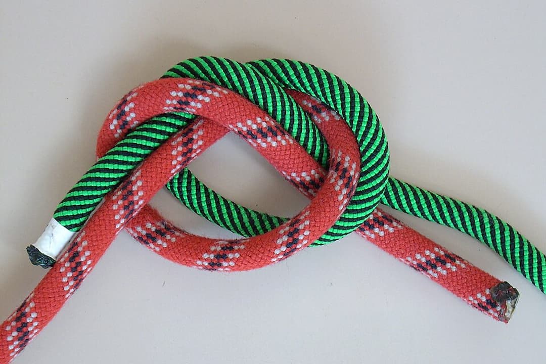 Red and green ropes tied together using a sheet bend knot on a light surface