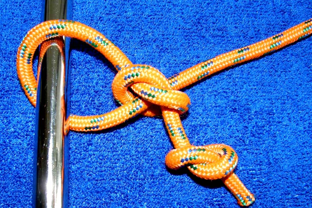 Orange braided rope tied in a uni knot around a shiny metal rod, displayed on a blue textured surface