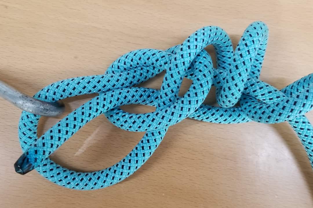 Rapala Loop Knot tied with a light blue braided rope through a metal eyelet, forming a strong non-slip loop on a wooden surface