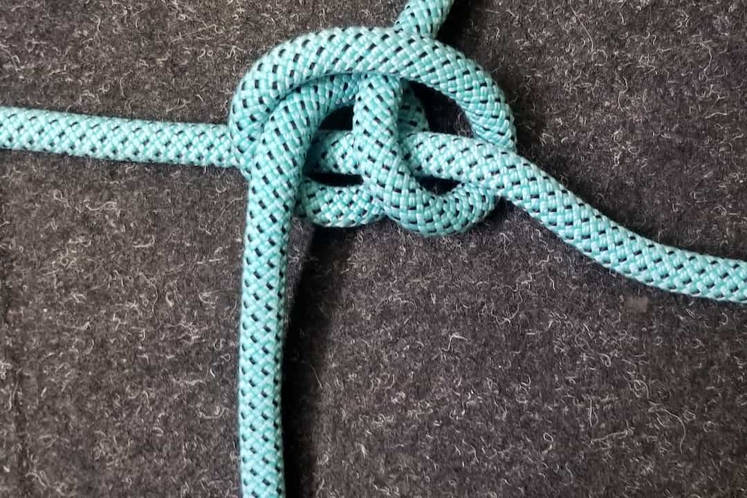 Blue braided rope tied in a round turn and two half hitches knot on a dark grey felt surface, forming a secure wrap and hitch combination