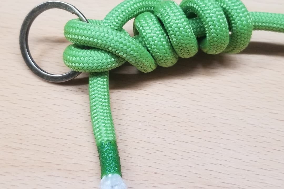 Green braided rope tied in a Trilene Knot around a metal ring, with multiple wraps forming a secure and compact coil, end neatly sealed with green tape