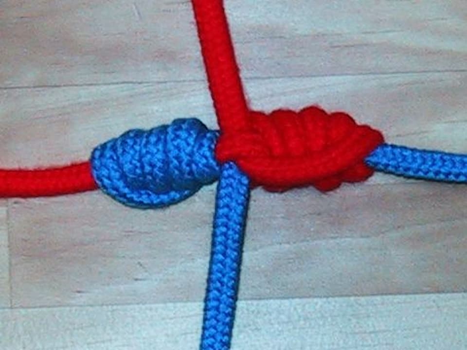 Blood Knot joining a red rope and a blue rope, tightly coiled and symmetrically wrapped on a wooden surface