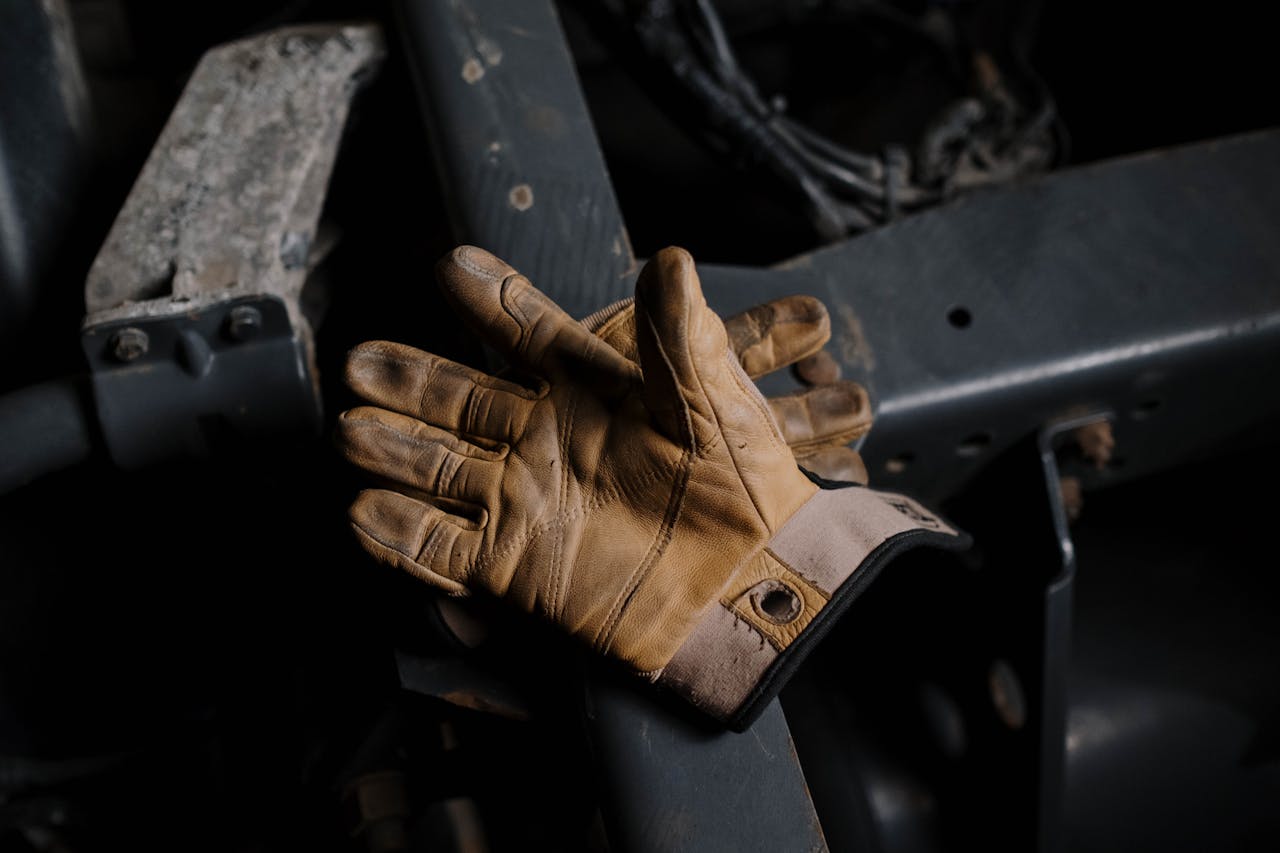 Brown leather work gloves resting on a piece of industrial metal machinery in a dimly lit setting