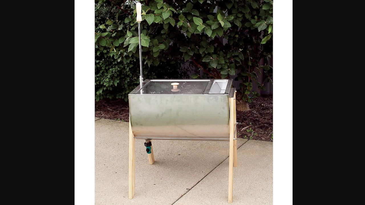 Stainless steel hand-crank laundry washer with wooden legs and a manual agitator handle, placed outdoors on a patio
