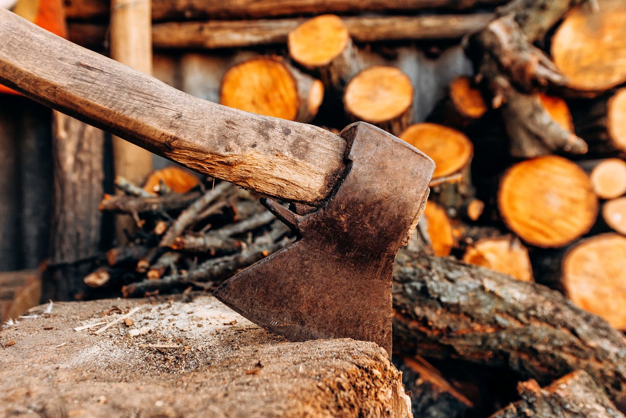 Old axe embedded in a tree stump with chopped firewood and logs stacked in the background