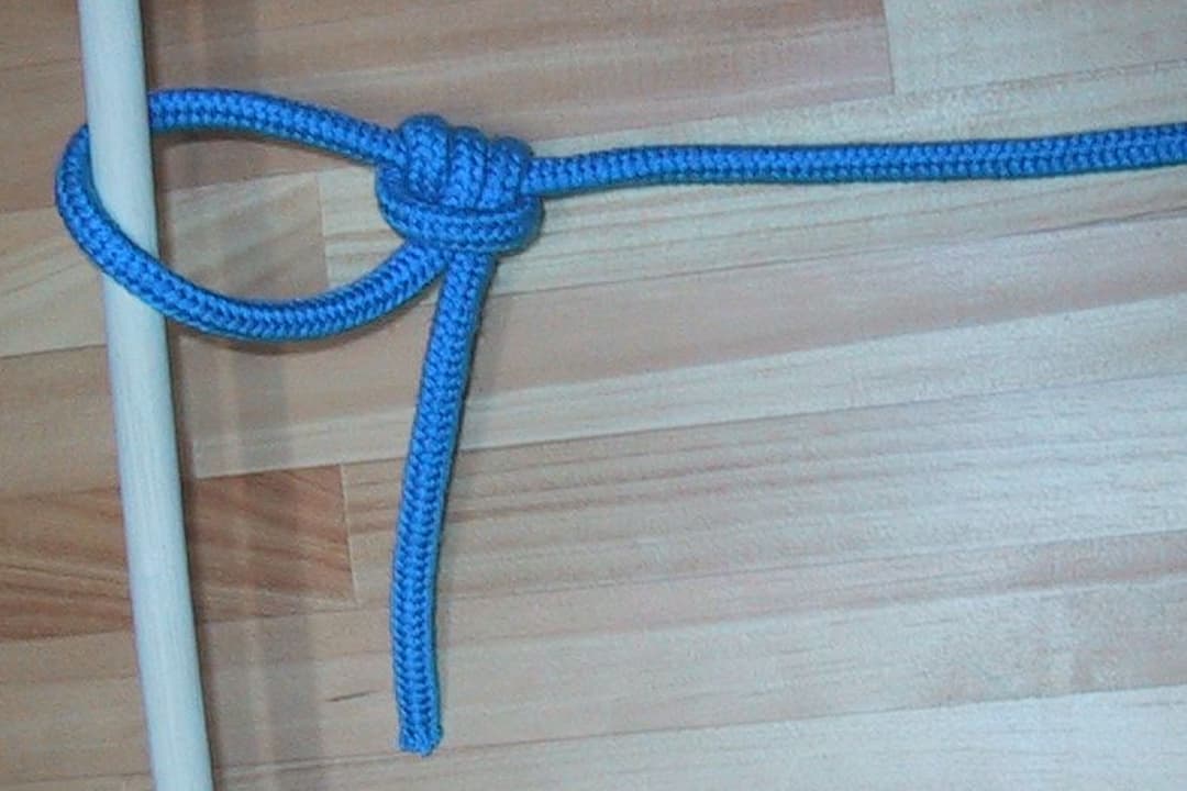 A taut-line hitch tied with a blue rope around a wooden pole on a light wooden floor