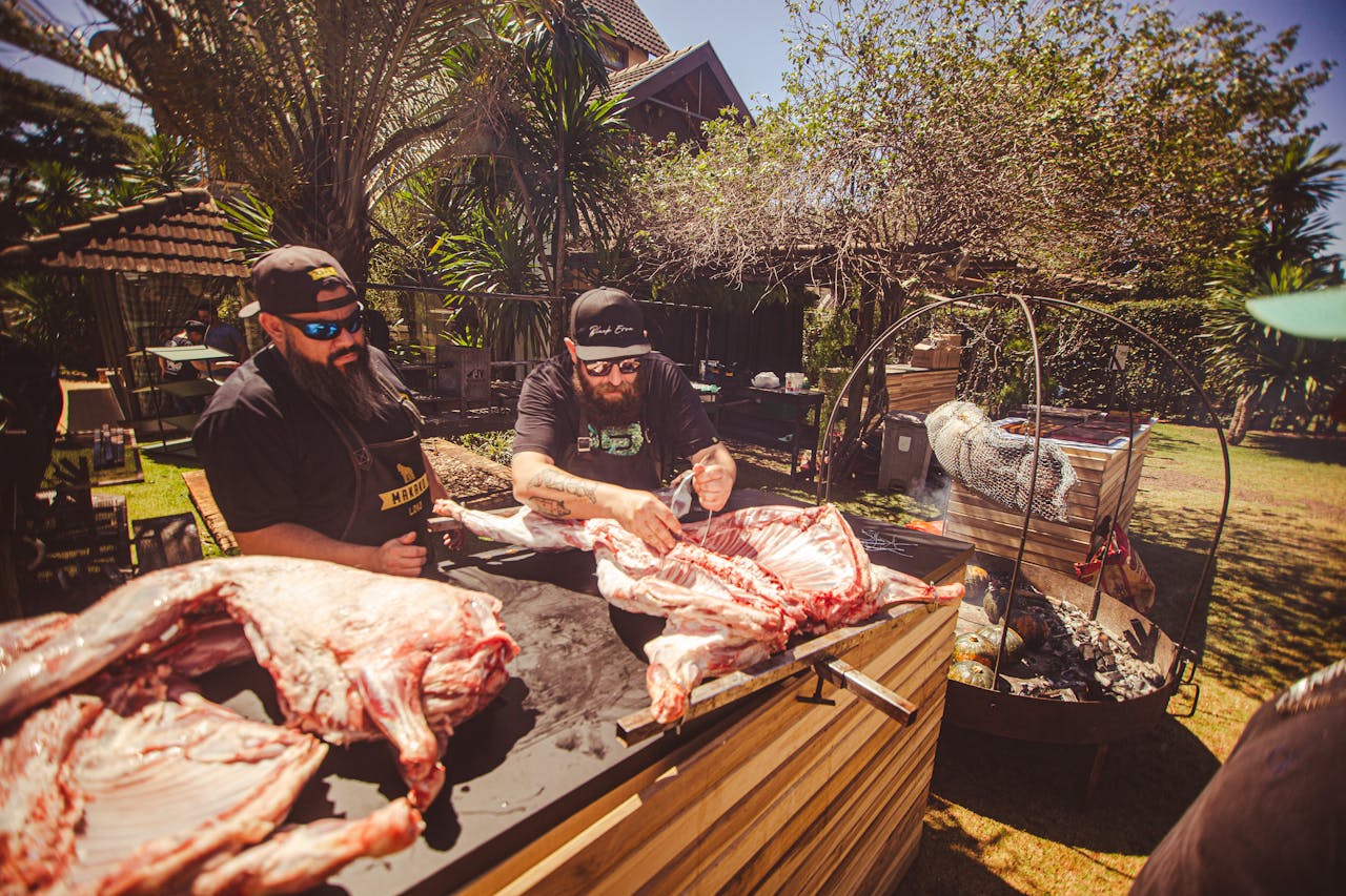 Two men butchering large animal carcasses at an outdoor setup on a sunny day