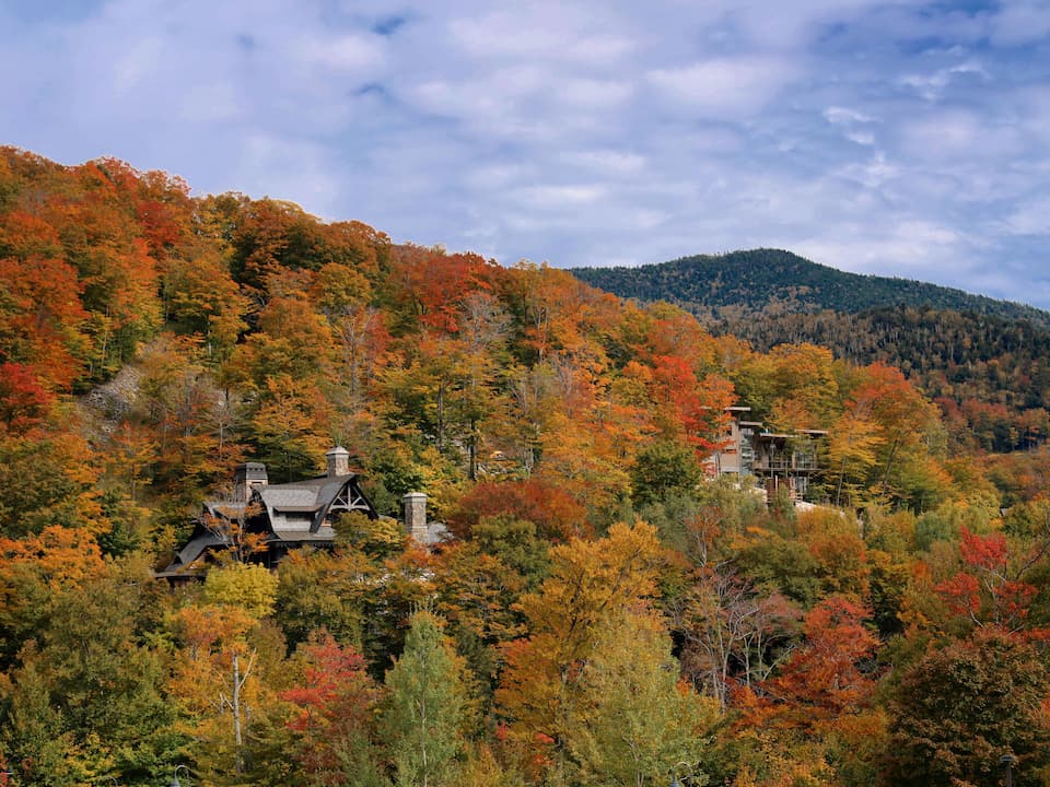 Large wooden mountain houses nestled among vibrant autumn trees with shades of red, orange, and yellow