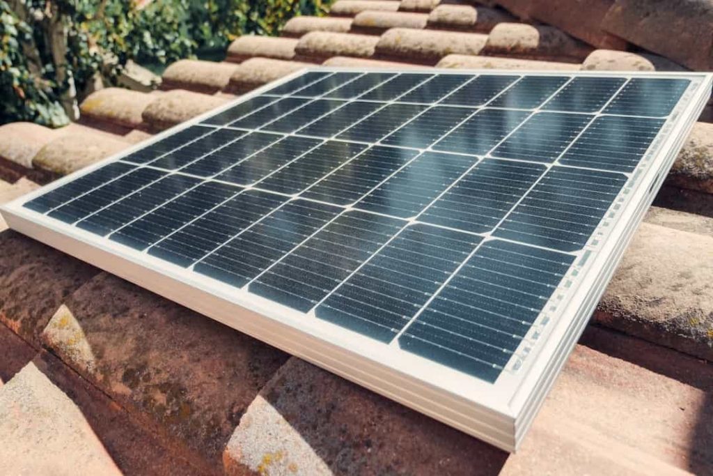 Solar panel placed on terracotta roof tiles, sunlight reflecting on the surface, greenery in the background
