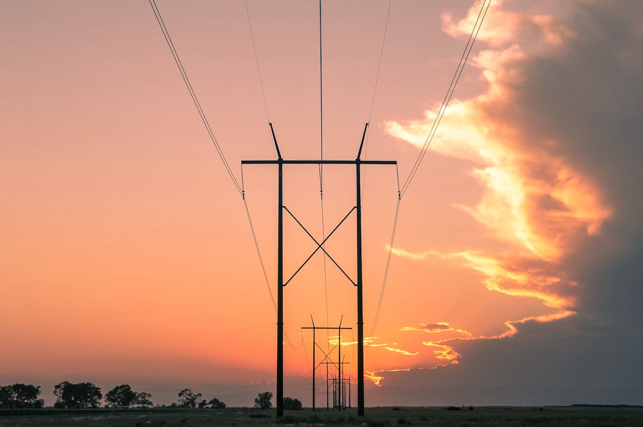 High-voltage power lines stretching across a rural landscape at sunset with vivid orange and purple sky