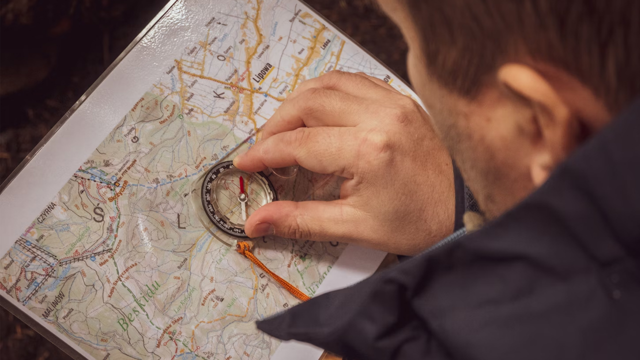 Person using a compass on a topographic map for navigation