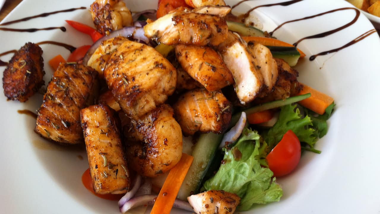 Grilled Cajun fish pieces served over a mixed vegetable salad on a white plate