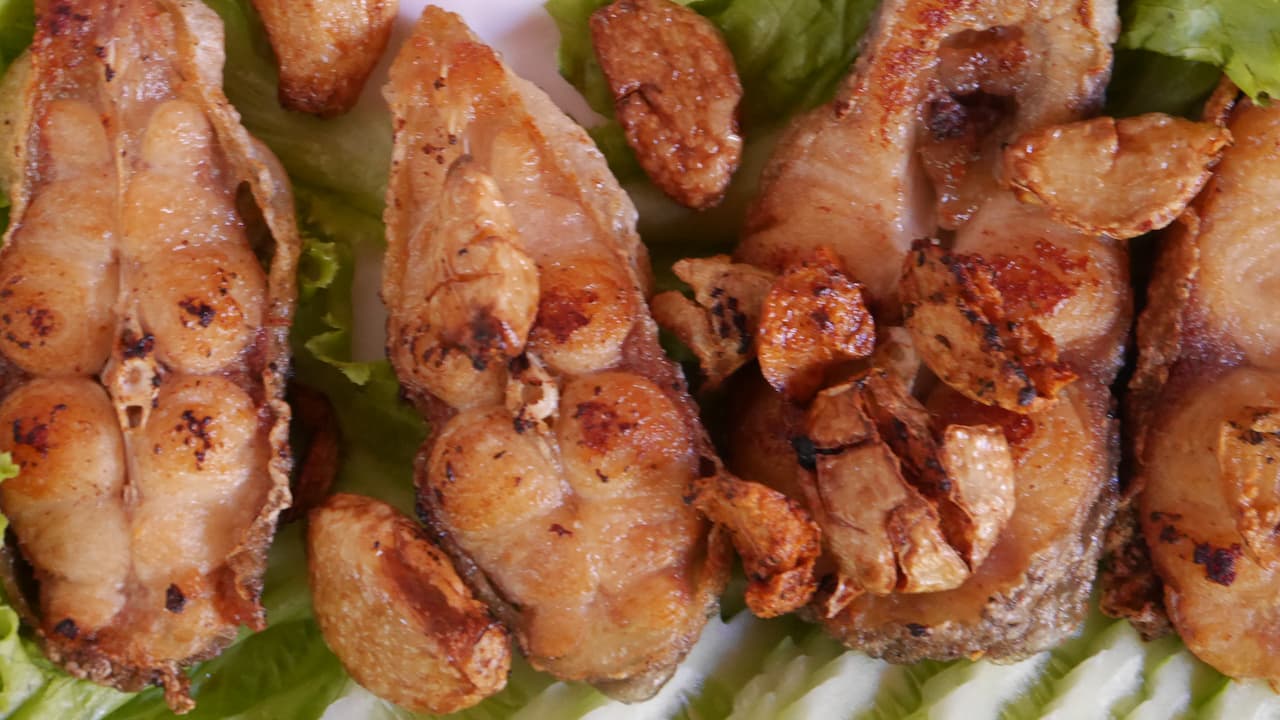 Grilled catfish fillets topped with crispy garlic slices on a bed of lettuce