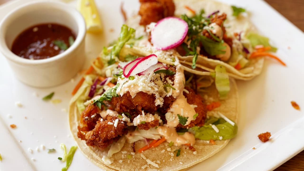 The image features two shrimp tacos served on soft corn tortillas